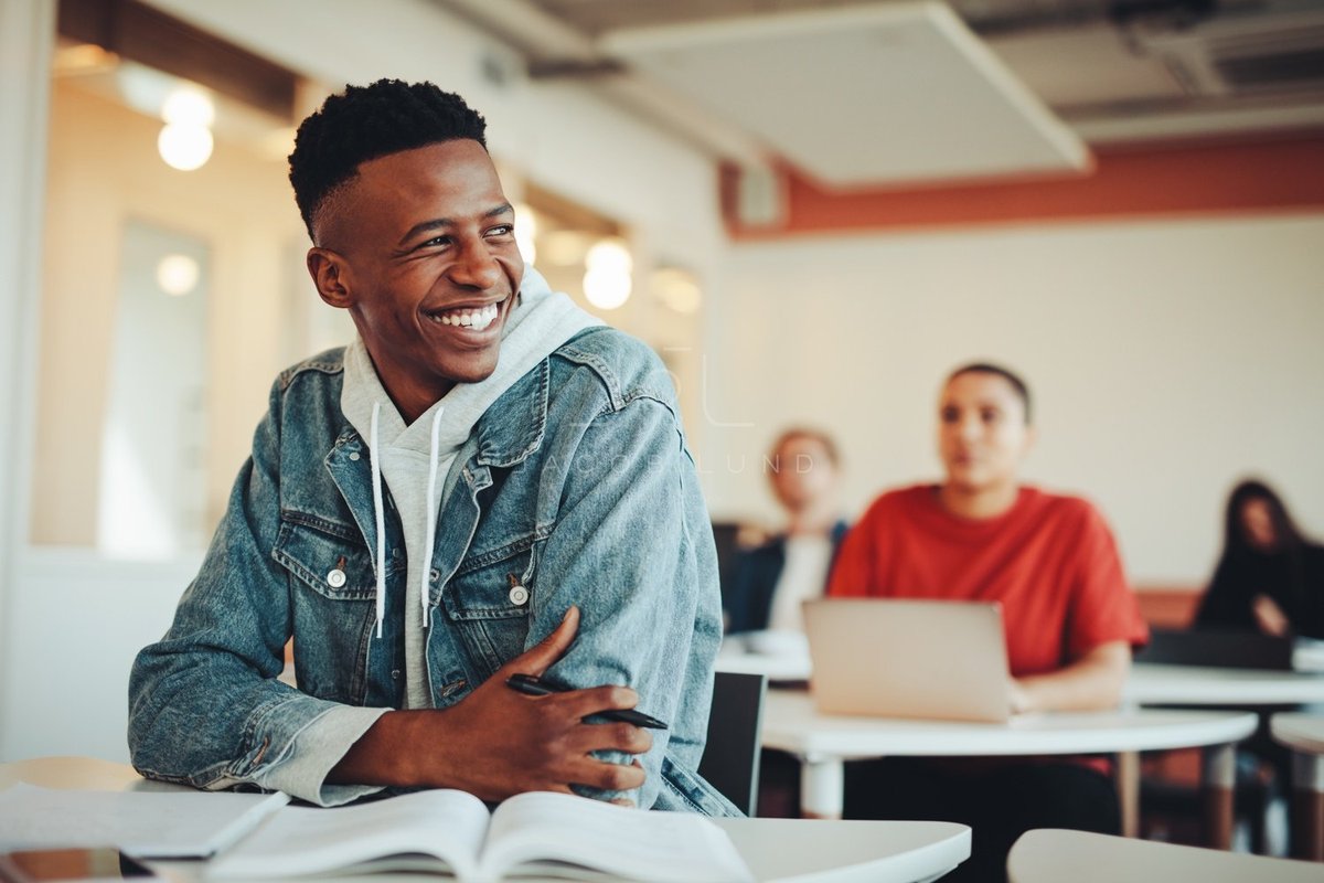 Um estudante pós-graduando sorrindo e olhando para o seu lado esquerdo, durante uma aula.
