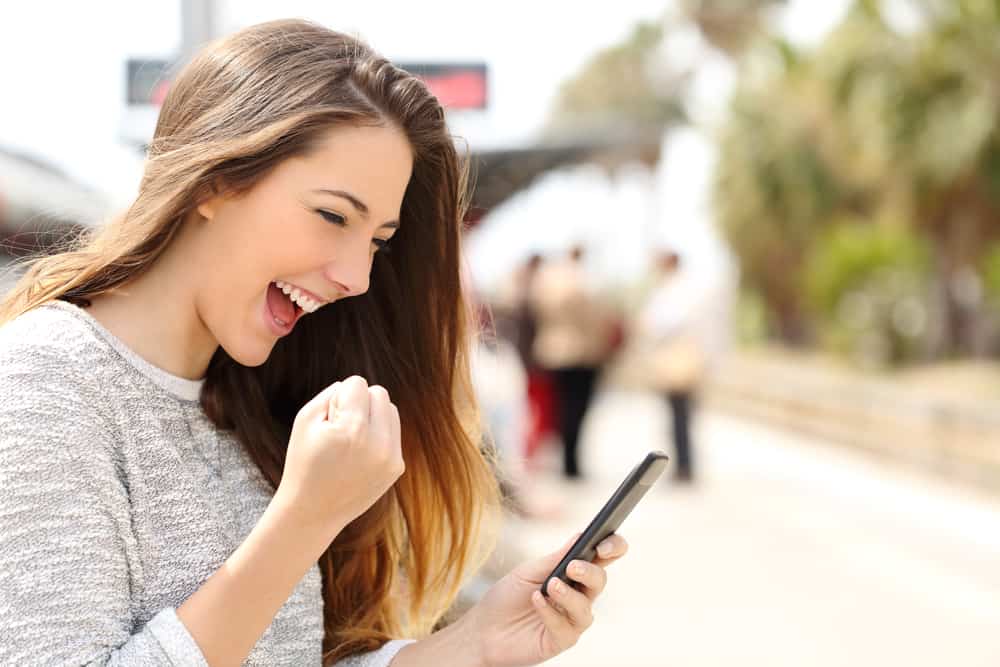Uma estudante pós-graduanda feliz olhando para o Joov, o melhor comparador de planos de saúde, no celular.