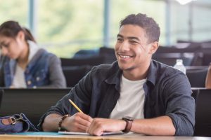 Estudante sorrindo em sala de aula com lápis em mãos.